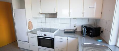 A compact kitchen with white cabinets, a stove, a toaster, and a sink.