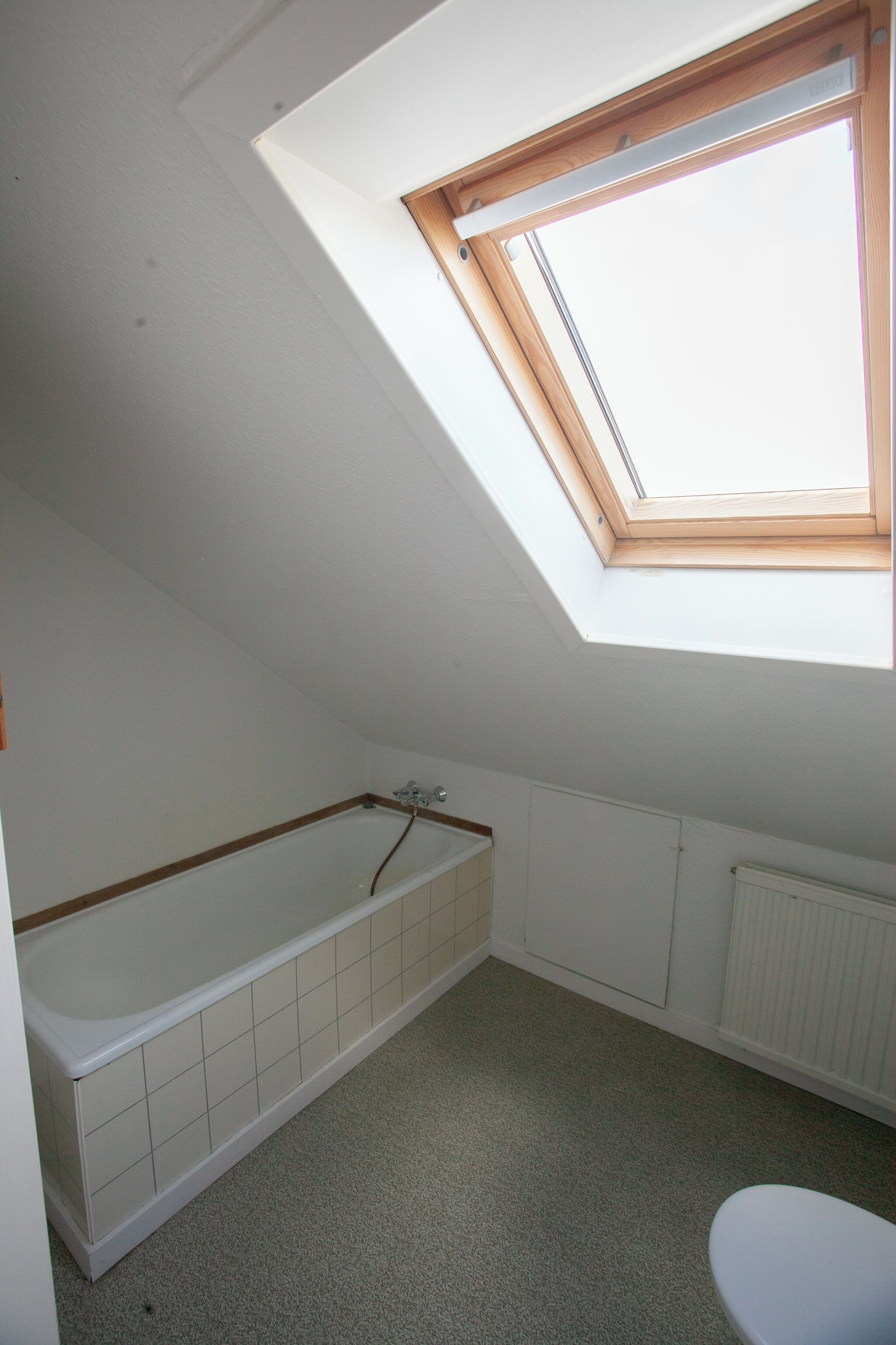 A small, narrow room with a skylight, a bathtub, and a toilet.