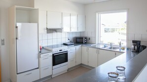 A modern kitchen with white cabinets, a microwave, stove, and a large window. - The Bird / Guesthouse / 10 Min Walk Downtown (Tórshavn)