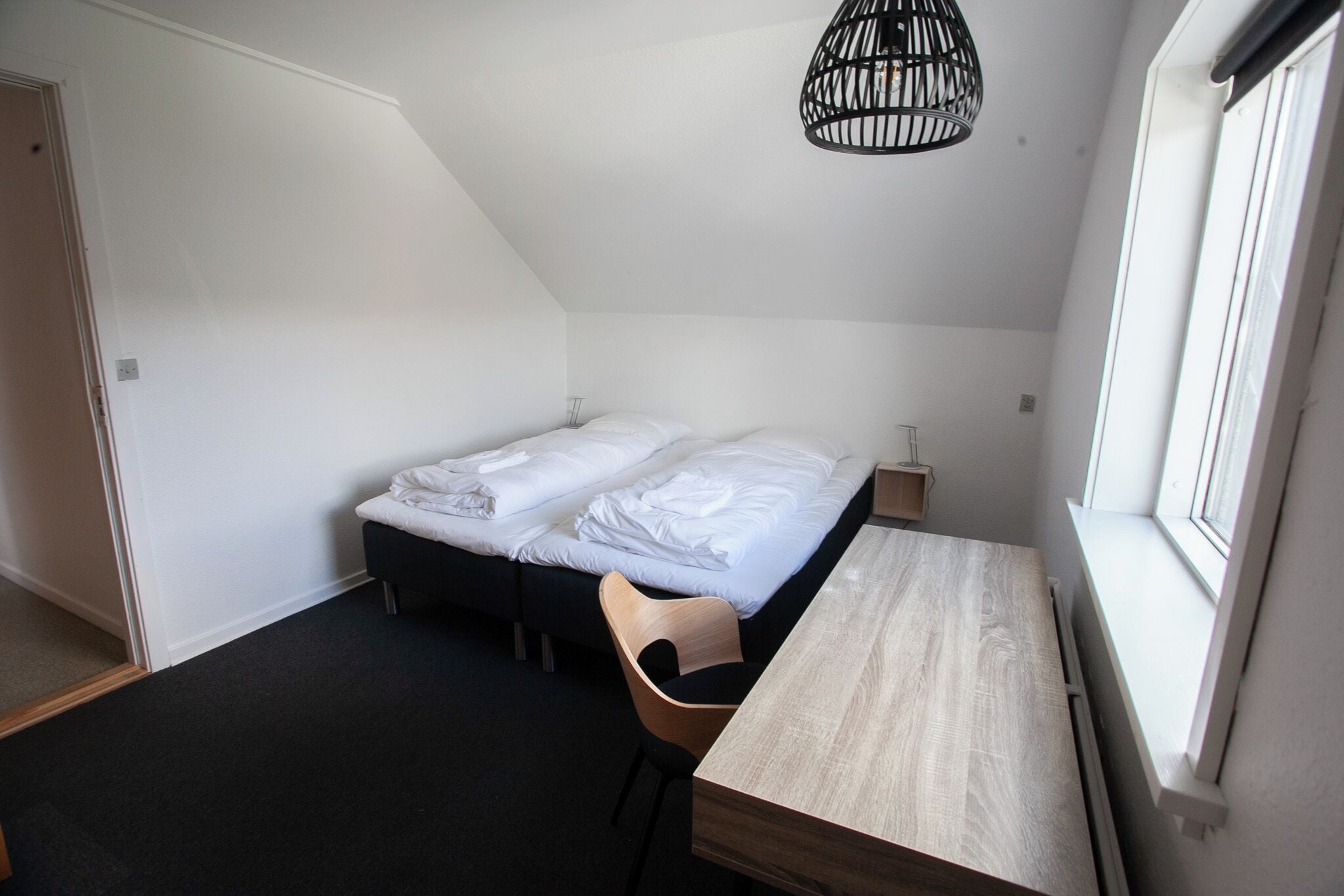 A small, modern bedroom with a single bed, a wooden desk, and a chair.