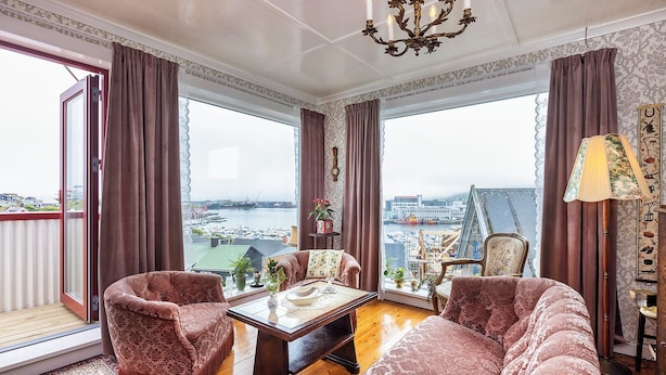 A spacious living room with a view of a harbor, featuring a sofa, armchairs, a coffee table, and a chandelier. - Downtown - Retro Decor - Stunning Views - Terrace (Tórshavn)