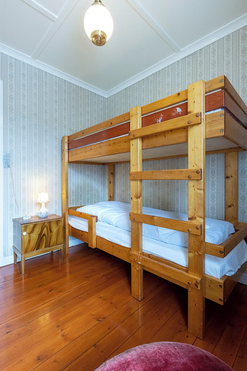 A bunk bed room with wooden construction, a nightstand with a lamp, and patterned wallpaper.