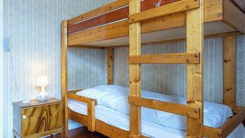 A bunk bed room with wooden construction, a nightstand with a lamp, and patterned wallpaper.