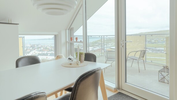 A modern dining area with a white table, black chairs, and a view of the city through large windows. - Stunning Views / Penthouse / Decorative / Parking (Nykobing Sjaelland)