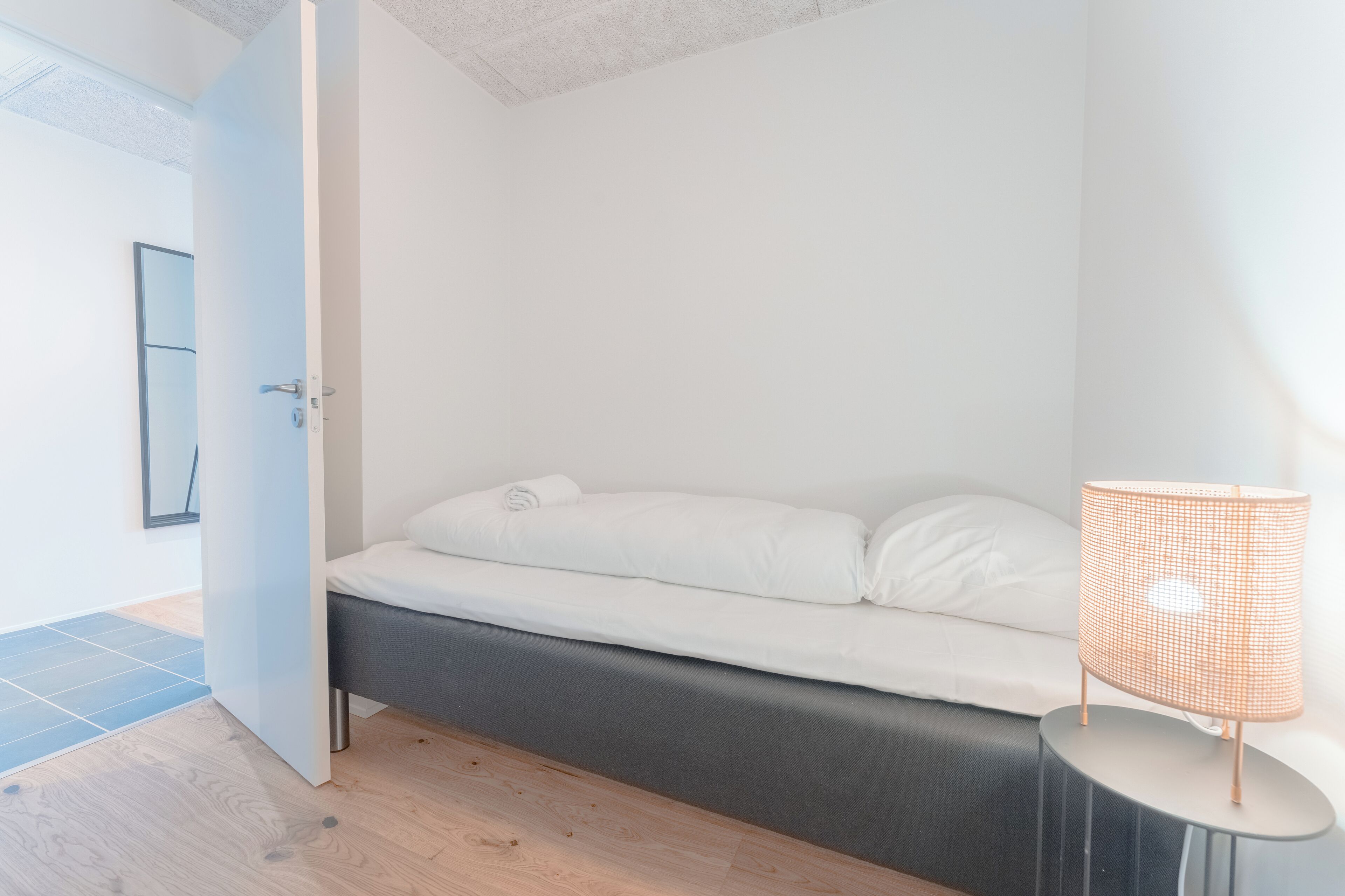 A modern bedroom with a bed, a bedside lamp, and a door leading to another room.