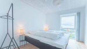 A modern bedroom with a large bed, bedside lamps, a standing lamp, and a view of the city through a large window.