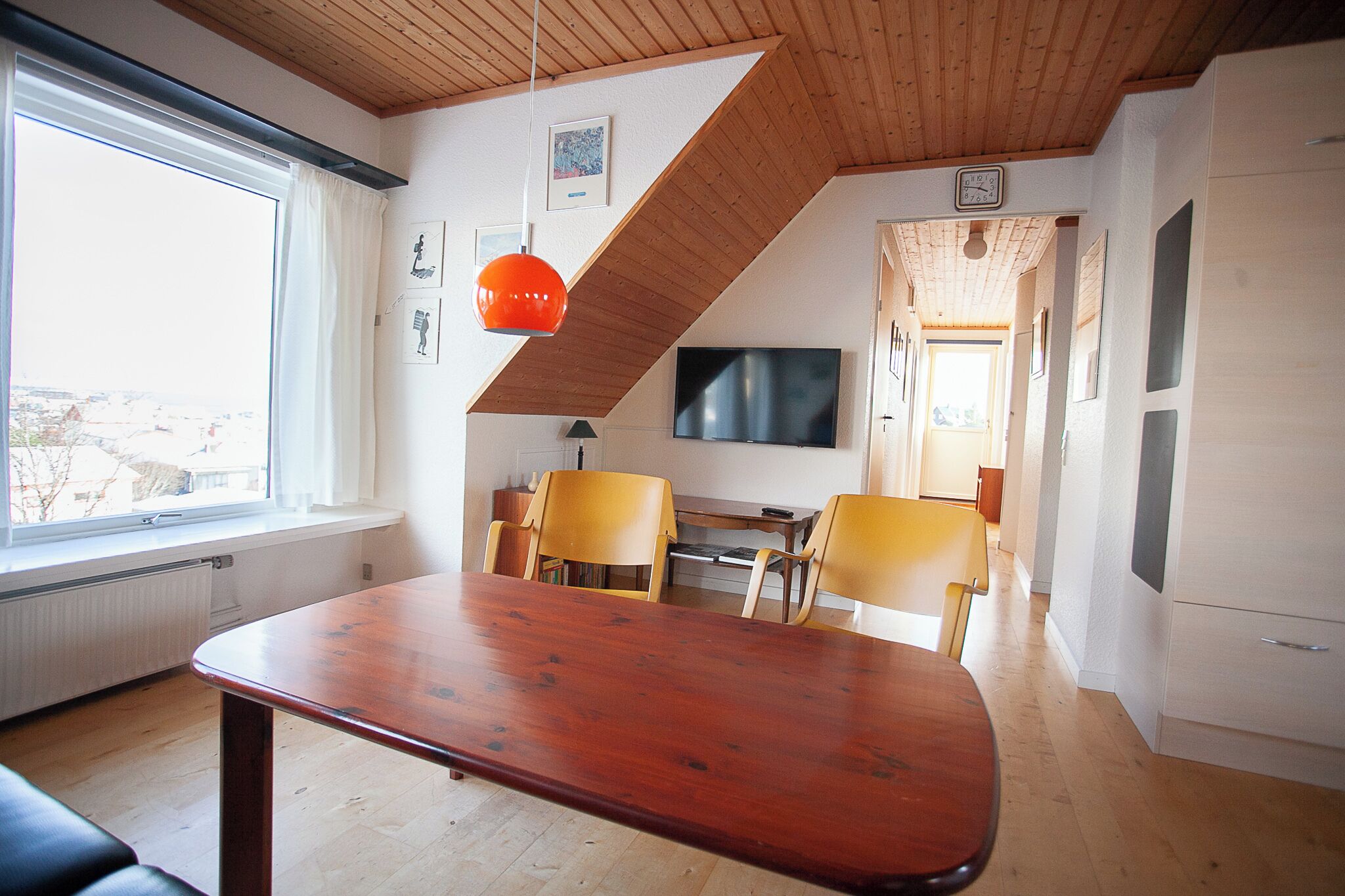 A dining area with a wooden table and chairs, a television, and a view of the city through a large window.
