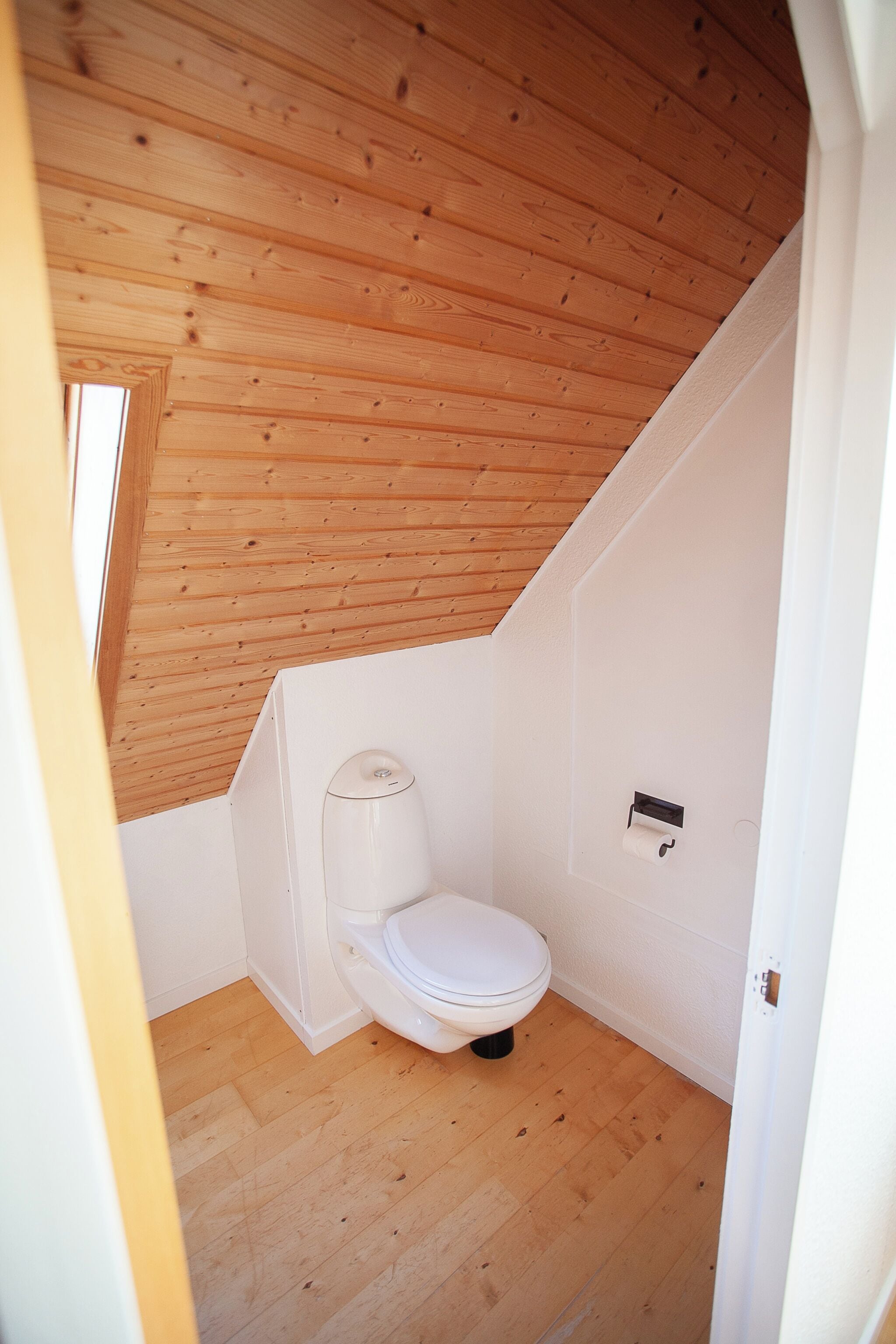 A small, compact bathroom with a wooden ceiling and white walls.