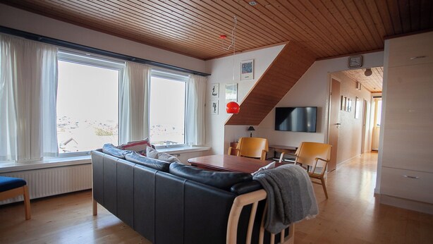 A modern living room with a wooden ceiling, a sofa, a dining table, and a TV. - Tórshavn - Central - City & Ocean Views - 3Br (Tórshavn)