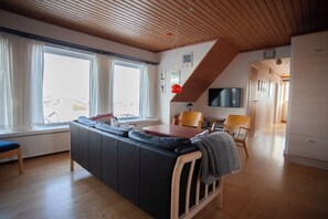 A modern living room with a wooden ceiling, a sofa, a dining table, and a TV. - Tórshavn - Central - City & Ocean Views - 3Br (Tórshavn)