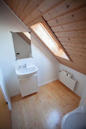 A small, clean bathroom with a wooden ceiling, a skylight, a white sink, and a toilet. - Tórshavn - Central - City & Ocean Views - 3Br (Tórshavn)