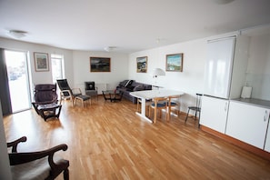 A spacious living area with a wooden floor, a dining table with chairs, a sofa, a small kitchen area, and a radiator. - Large Apartment With Fabulous View Of Tórshavn (Tórshavn)
