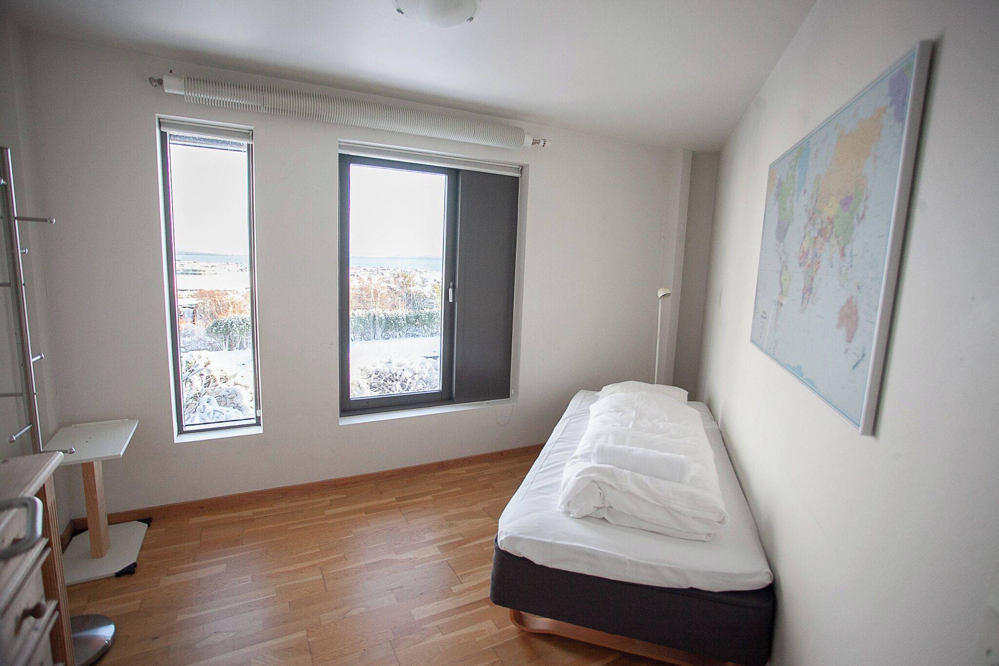 Quarto com cama, duas janelas, mapa na parede e piso de madeira.