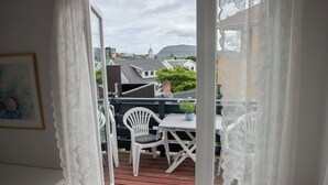 A room with a white chair, a small table, and a view of a balcony with outdoor furniture.