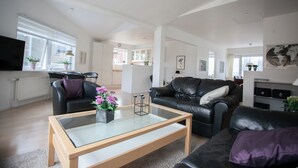 A modern living room with a glass coffee table, leather sofas, and a view of the kitchen and dining area. - Downtown Tórshavn - Large 3 Bedroom Apartment (Tórshavn)
