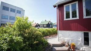 Ein rotes Haus mit weißen Verzierungen, einer Holzterrasse und Blumentöpfen.
