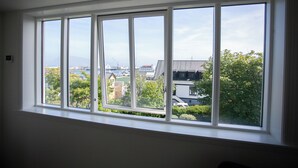 Ein Zimmer mit einem großen Fenster und Blick auf einen Hafen mit Gebäuden und Grünflächen.