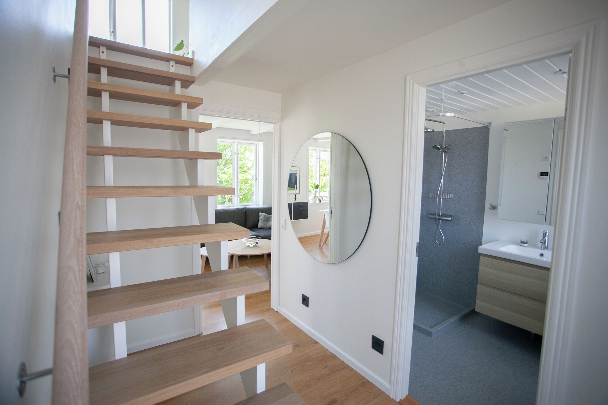 A modern interior with a wooden staircase, a round mirror, and a shower area.
