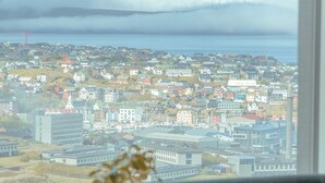 A room with a large window offering a view of a cityscape and a body of water. - Breathtaking Views - New - 220M2 - 5 Br - Walks (Argir)