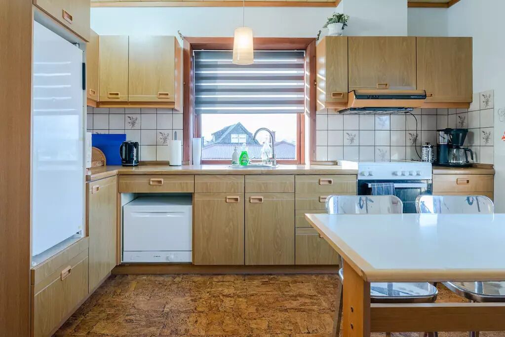 Une cuisine compacte avec des meubles en bois, un lave-vaisselle encastré, une cuisinière et une fenêtre donnant sur une maison.