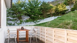 A small outdoor seating area with a table and chairs, surrounded by a wooden fence and a view of trees and a hillside. - 3 Bedroom Apartment / Great Sea View / Quiet (Argir)