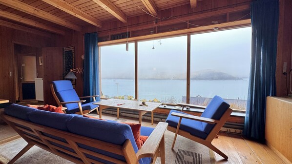 A room with a large window, wooden furniture, and a view of the sea.