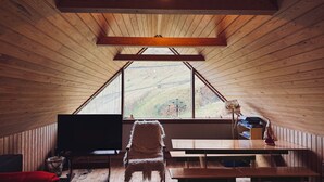A cozy cabin with a wooden interior, a large window offering a view of a hillside, a television, and a dining area. - Idyllic Vacation Home With A Breathtaking View (Bøur)