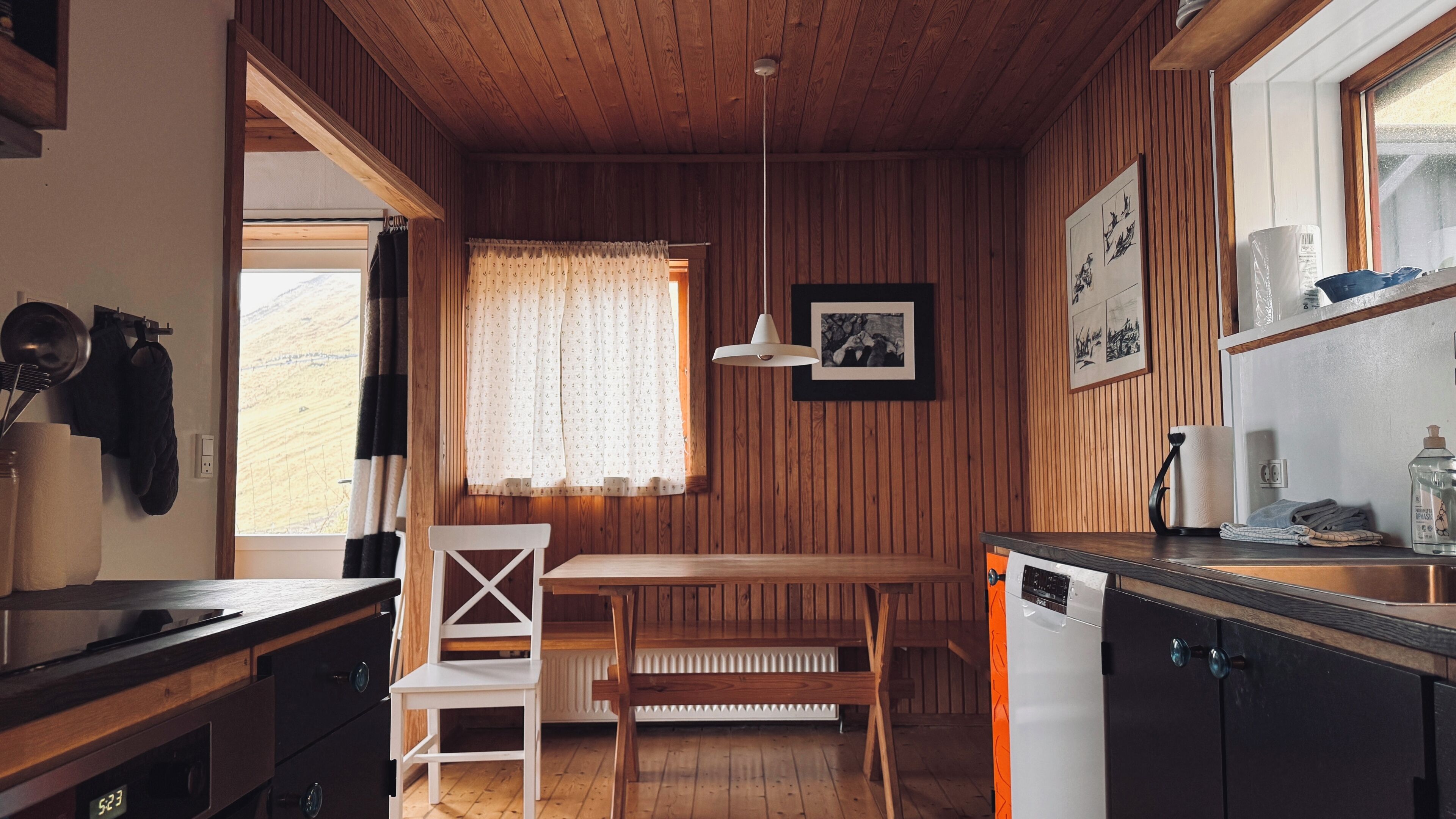 A wooden-paneled room with a kitchen area, a dining table, and a white chair.