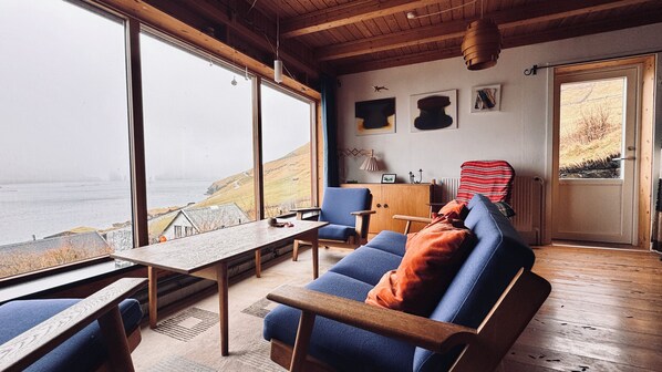 A cozy cabin with a large window overlooking a scenic view, a wooden table, a blue sofa, and a chair.