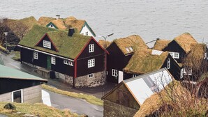 A row of houses with thatched roofs, a street, and a body of water in the background. - Idyllic Vacation Home With A Breathtaking View (Bøur)