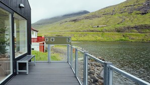 A wooden deck with a railing overlooking a body of water and hills.