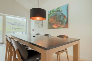 A dining area with a long table, chairs, a pendant light, and a fish painting on the wall. - A Pearl In A Forgotten Fjord - Luxury Boathouse (Funningsfjørður)