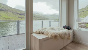A room with large windows overlooking a lake and hills, a fur throw on a bench, and a lamp on a windowsill.