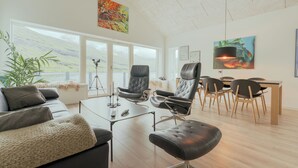 A modern living room with a sofa, armchairs, a coffee table, and a dining area with chairs and a table.