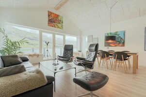 Ein modernes Wohnzimmer mit einer Couch, Sesseln, einem Couchtisch und einem Essbereich mit Stühlen und einem Tisch.