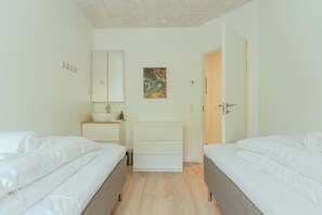 A bedroom with two beds, a bedside table, a dresser, a mirror, and a door leading to another room. - A Pearl In A Forgotten Fjord - Luxury Boathouse (Funningsfjørður)
