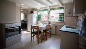 A compact kitchen with a stove, refrigerator, and a dining table with chairs. - Cozy House In The Idyllic Village Of Haldórsvík (Haldórsvík)