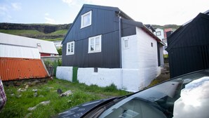 A two-story building with a dark and white exterior, surrounded by other buildings and a car. - Cozy House In The Idyllic Village Of Haldórsvík (Haldórsvík)