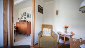 A cozy room with a wooden floor, a chair with a patterned cushion, a small table with a vase, and a cabinet with framed photos. - Cozy House In The Idyllic Village Of Haldórsvík (Haldórsvík)