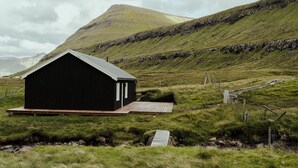 A black building with a sloped roof in a grassy area with a mountain in the background. - Authentic Cabin - Unique Location - In Nature - 2Br (Hellurnar)
