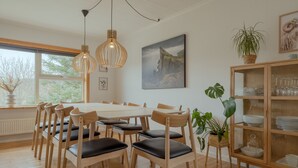 A dining area with a wooden table and chairs, a hanging light fixture, a painting, and a cabinet with glass doors. - Unique Location - Bodanes - Hoydalar - 6 Br Villa (Hoyvík)