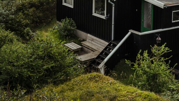 A black house with a green door, a small porch, and a view of the sea and mountains. - Cottage With Stunning View Of The Sea And Islands. (Leynar)