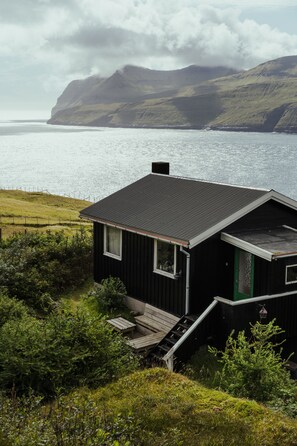 A black house with a green door, a small porch, and a view of the sea and mountains. - Cottage With Stunning View Of The Sea And Islands. (Leynar)
