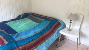 A bed with a colorful quilt, a white chair, and a lamp. - Cottage With Stunning View Of The Sea And Islands. (Leynar)