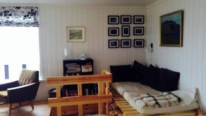 A room with a wooden bench, a sofa, a chair, and a bookshelf against the wall. - Cottage With Stunning View Of The Sea And Islands. (Leynar)