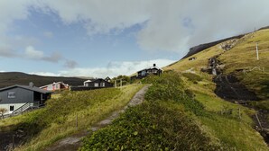 A rural landscape with houses on a hillside, a gravel path, and a small stream. - Cottage With Stunning View Of The Sea And Islands. (Leynar)