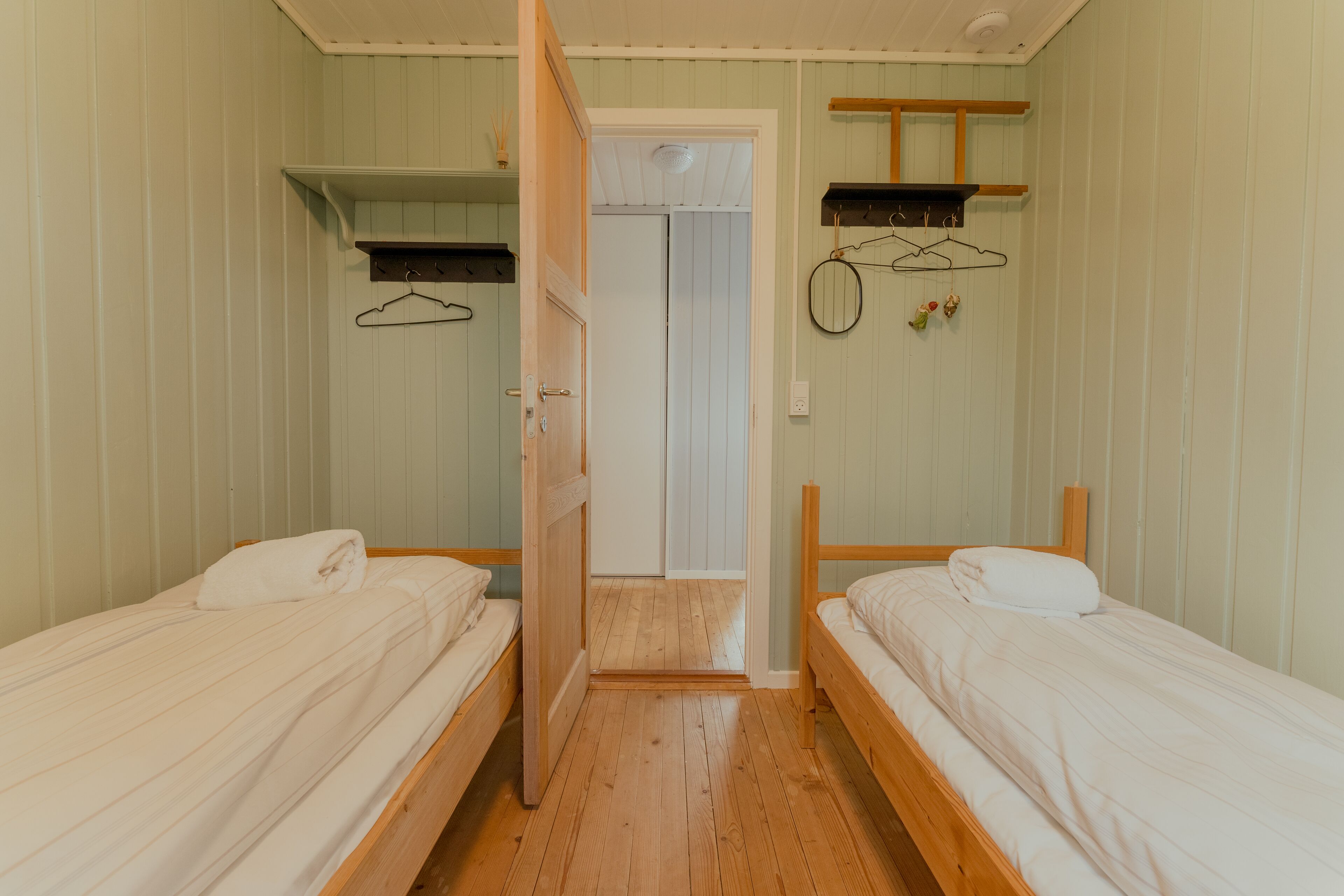 A room with two wooden beds, a wooden door, a shelf, and a wall-mounted rack with hangers.