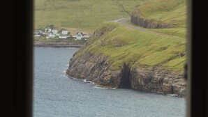A coastal landscape with houses on a hillside, a road, and a body of water.