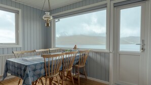 A dining area with a table set for four, wooden chairs, a patterned tablecloth, and a view of the sea through large windows.