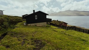 A black house with a small porch, a red barn, and a grassy area with a path leading to the house.